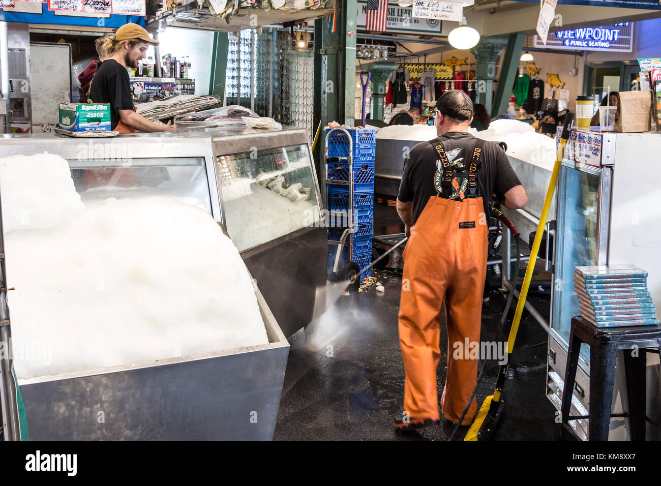 Seattle, Washington, Stati Uniti d'America - 4 settembre 2017: lavoratore di sesso maschile che indossa un impermeabile pantaloni di pesca è la pulizia del pavimento a Pike Place pesce con un pressur Foto Stock