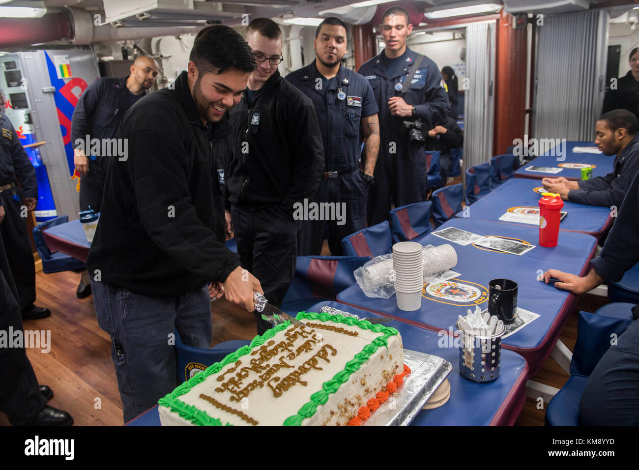 Cryptologic Technician (Collection) terza classe Jared Ammon, di Salyer, California, taglia la torta per celebrare il mese del patrimonio dei nativi americani della Marina a bordo del cacciatorpediniere guidato della classe Arleigh Burke USS Mustin (DDG 89). Mustin opera come parte del Ronald Reagan Strike Group nella settima area operativa della flotta degli Stati Uniti, una forza pronta per il combattimento che protegge e difende l'interesse marittimo collettivo dei suoi alleati e partner nell'Indo-Asia-Pacifico. (STATI UNITI Navy Foto Stock