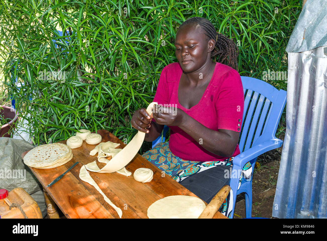 Keniote africana Luo donna seduta all'aperto preparazione chapattis mediante laminazione della pasta, Kenya, Africa orientale Foto Stock