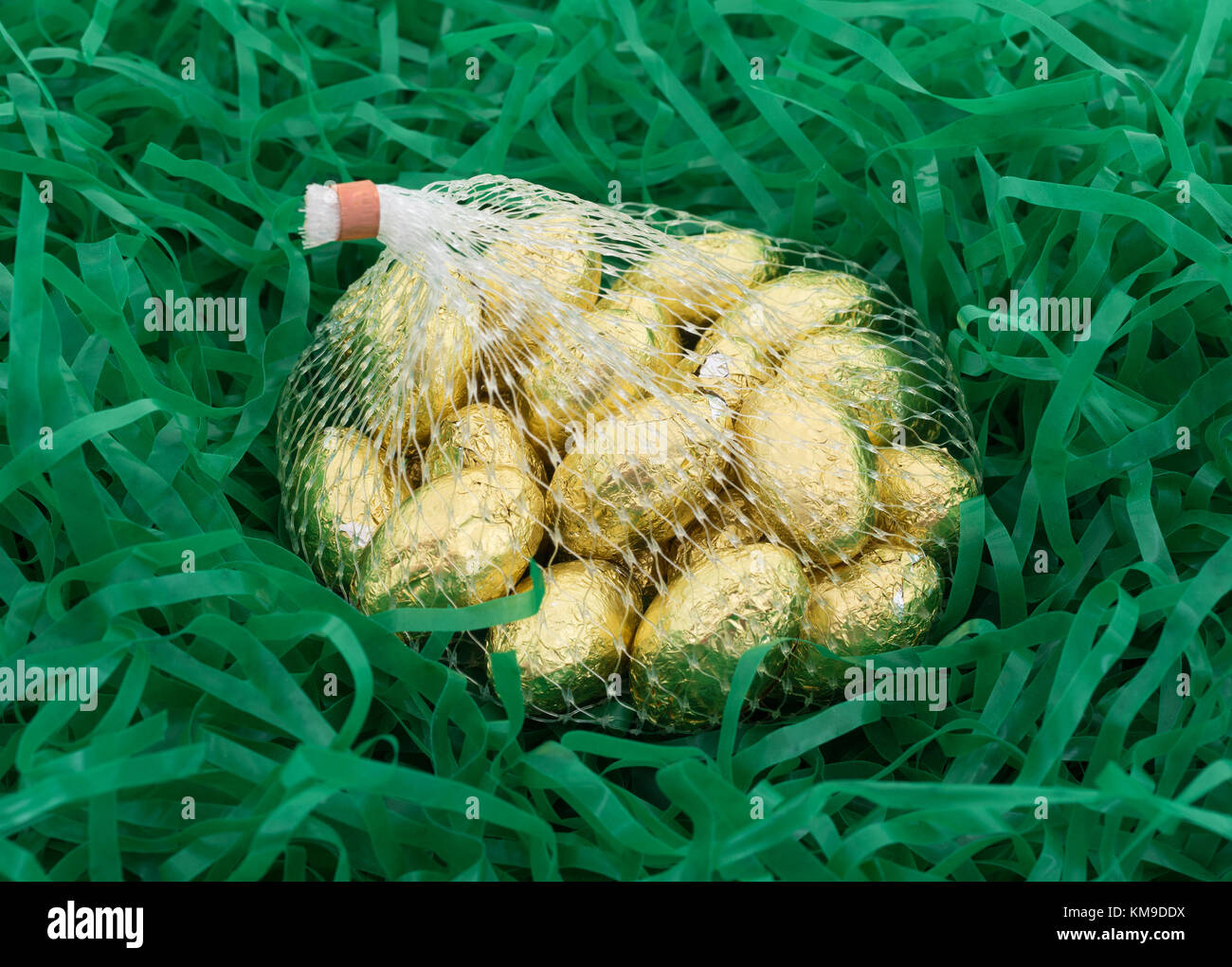 Una borsa a rete di lamina di oro avvolto di pasqua di cioccolato candy uova in plastica tagliuzzata erba verde. Foto Stock