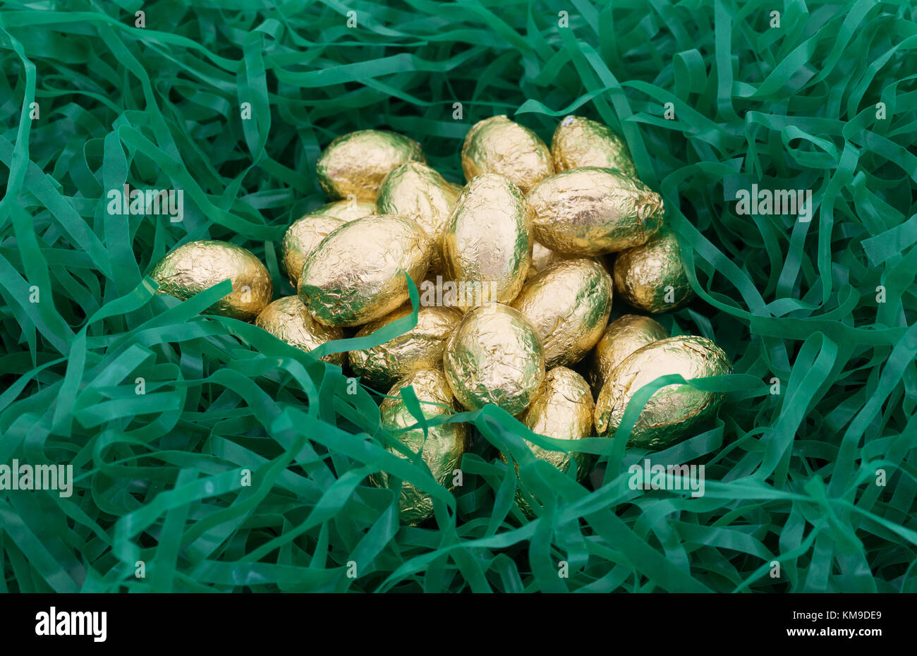 Un mucchio di lamina di oro avvolto di pasqua di cioccolato uova candy annidato in plastica tagliuzzata erba verde. Foto Stock