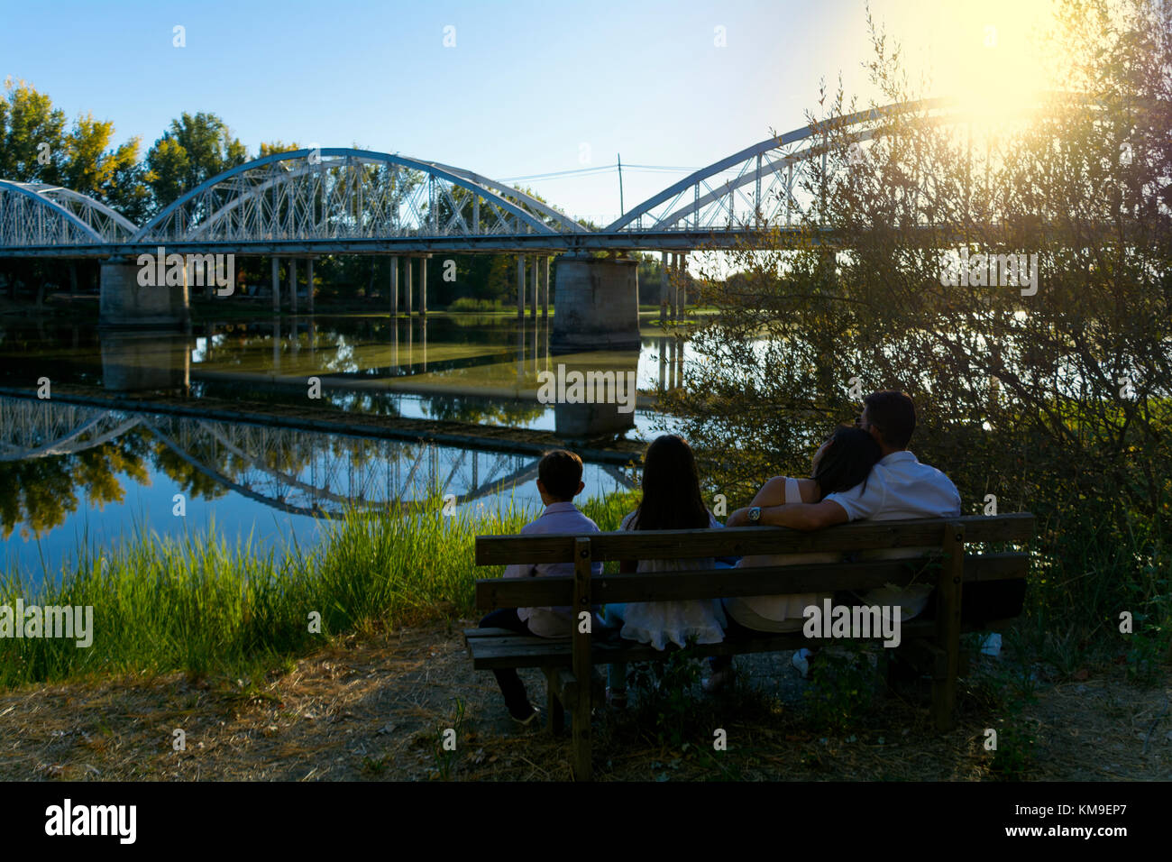 Famiglia con due figli azienda seduta su una panchina da un fiume Foto Stock