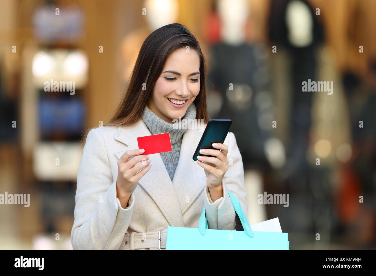 Felice Tiene shopper shopping bags pagare on line con un telefono e una carta di credito sulla strada in inverno Foto Stock