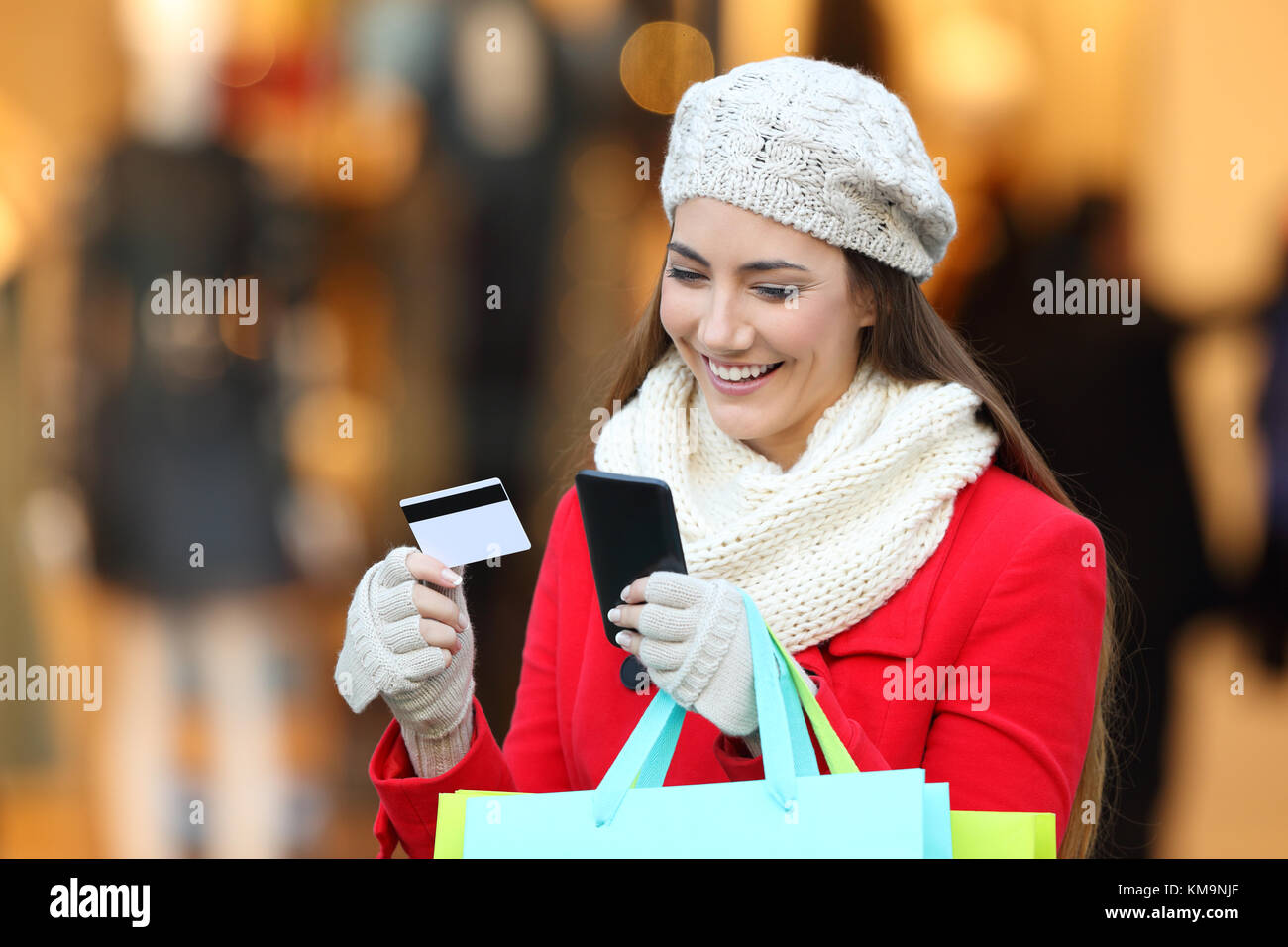 Happy shopper pagare on line con telefono e carta di credito su strada in inverno con un storeftont in background Foto Stock