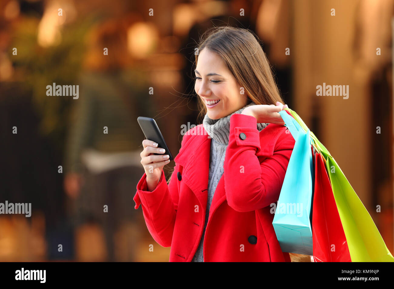 Happy shopper indossando un cappotto rosso shopping e utilizzando una smart phpone sulla strada in inverno Foto Stock