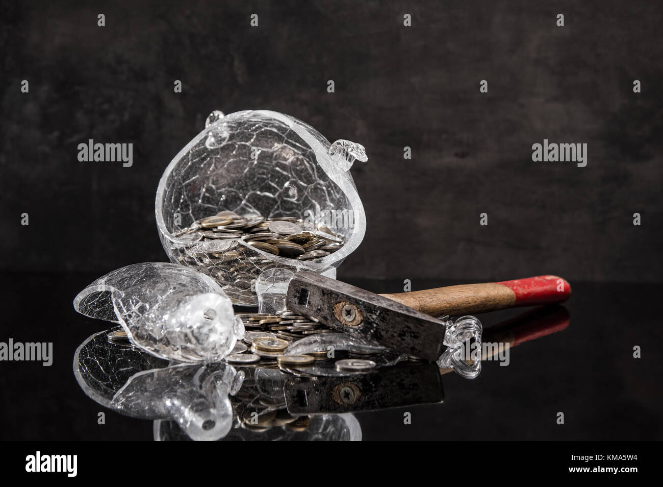 Schiacciato salvadanaio con monete e un martello su sfondo scuro Foto Stock