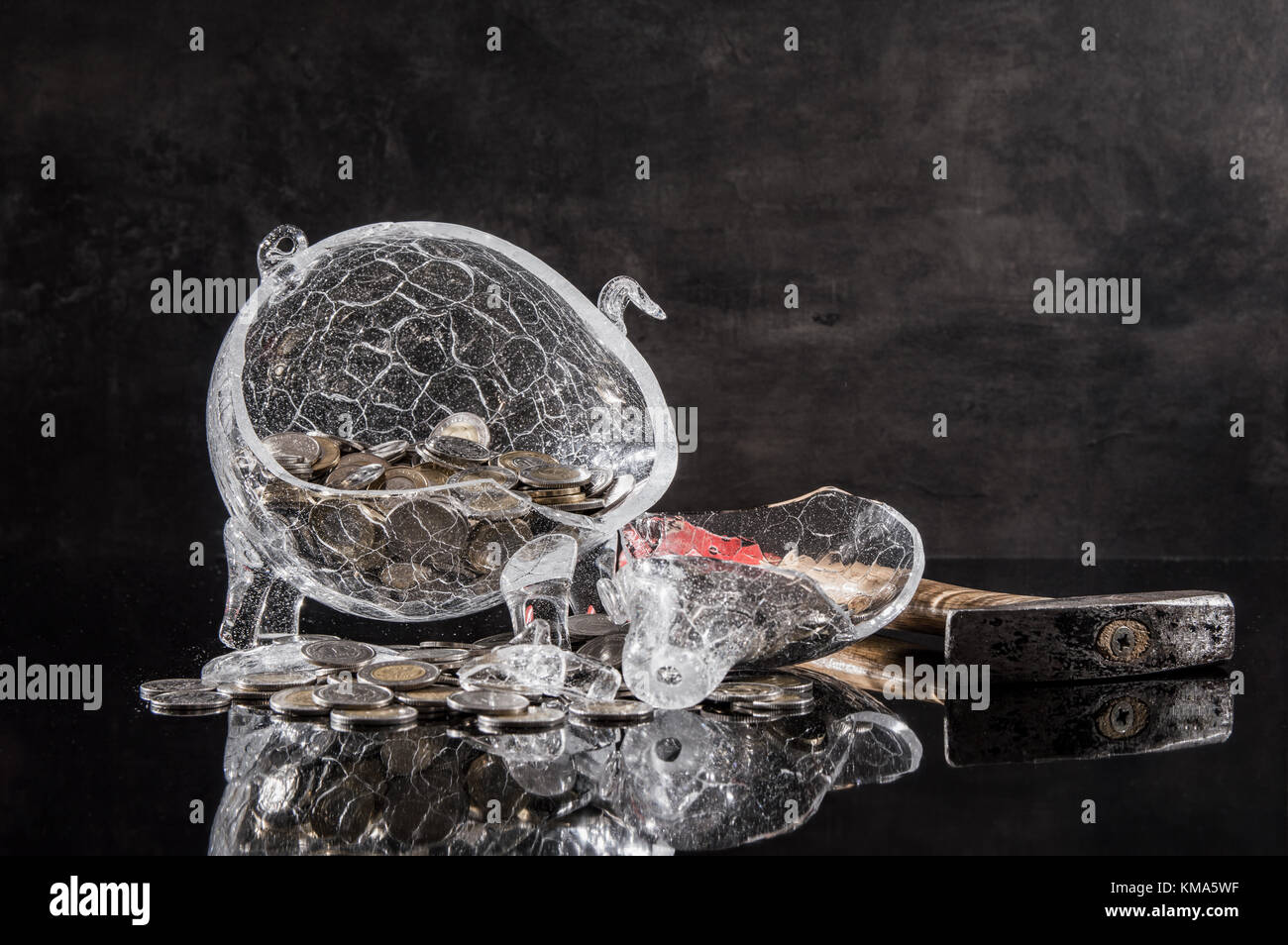 Schiacciato salvadanaio con monete e un martello su sfondo scuro Foto Stock