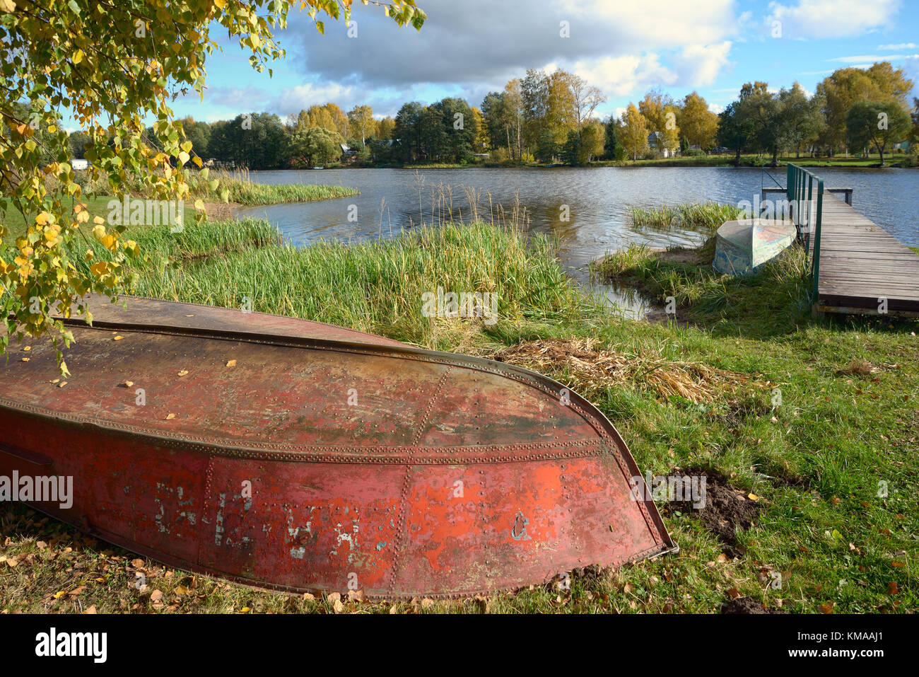 Due invertiti in ferro e in barca dal molo di legno sul fiume con Giallo autunno alberi contro lo sfondo Foto Stock