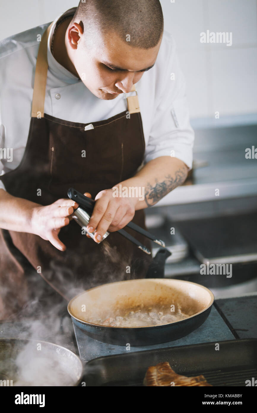 Giovane maschio attraente cook con uniforme di preparare piatti deliziosi. Foto Stock