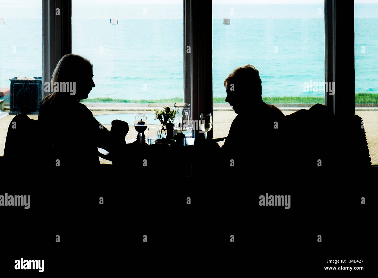 Due donne viste in silhouette sedute accanto a una finestra in un ristorante. Foto Stock
