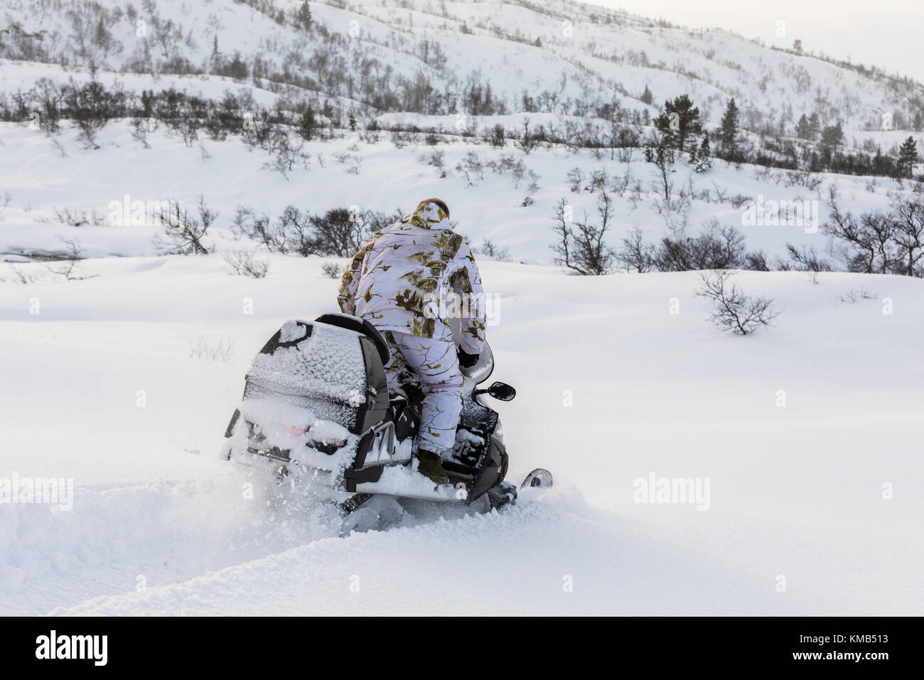 L'uomo che indossa abbigliamento camouflage invernale guida una motoslitta  nella neve sulla montagna in Norvegia Foto stock - Alamy