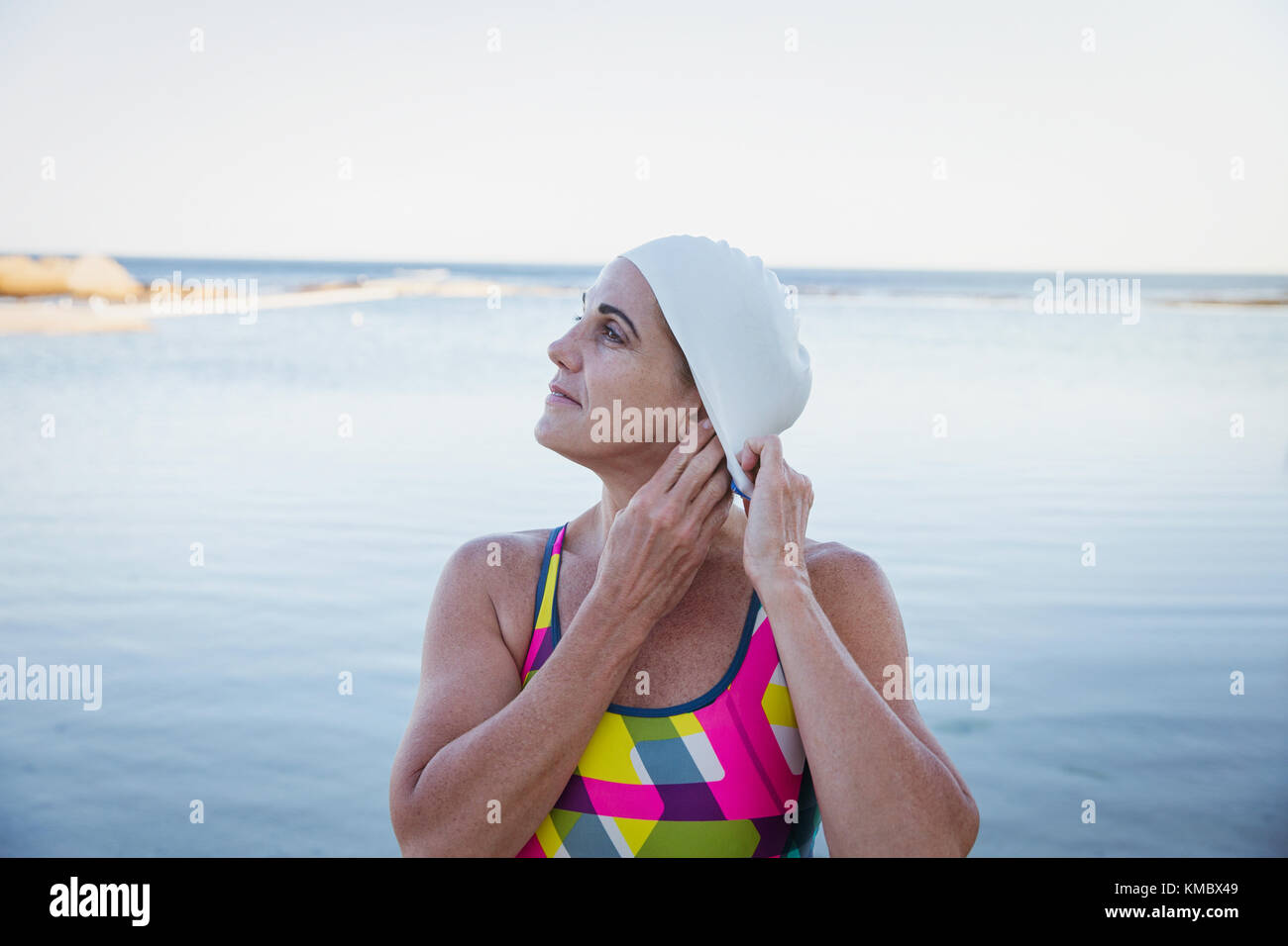 Nuotatore femminile ad acqua aperta che attorcigliano i capelli nella cuffia da bagno surf oceano Foto Stock