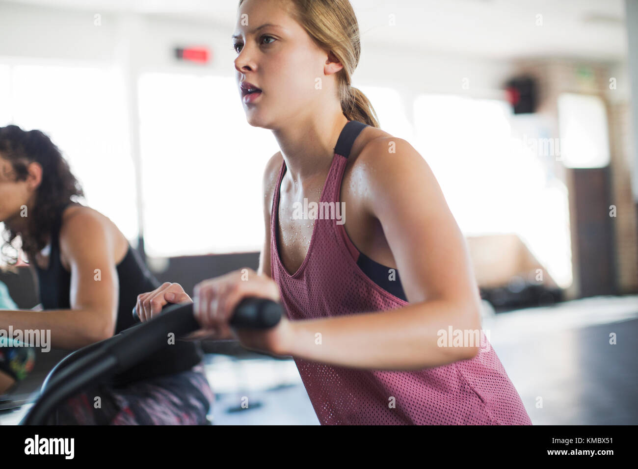 Determinata giovane donna che usa la bicicletta ellittica in palestra Foto Stock