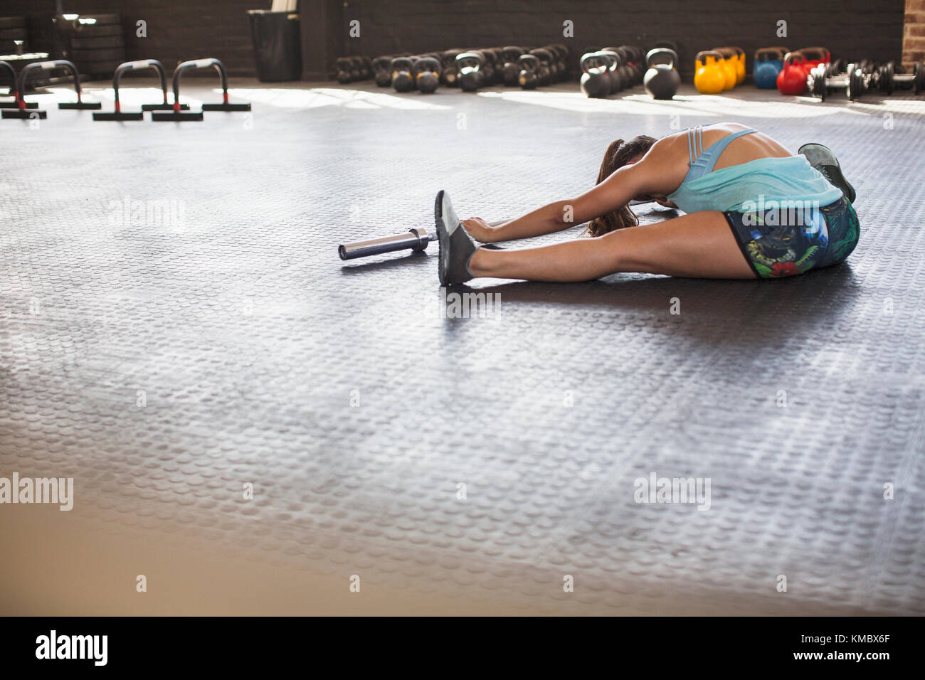 Giovane donna che si allunga, facendo avanti piega usando il barbell in palestra Foto Stock