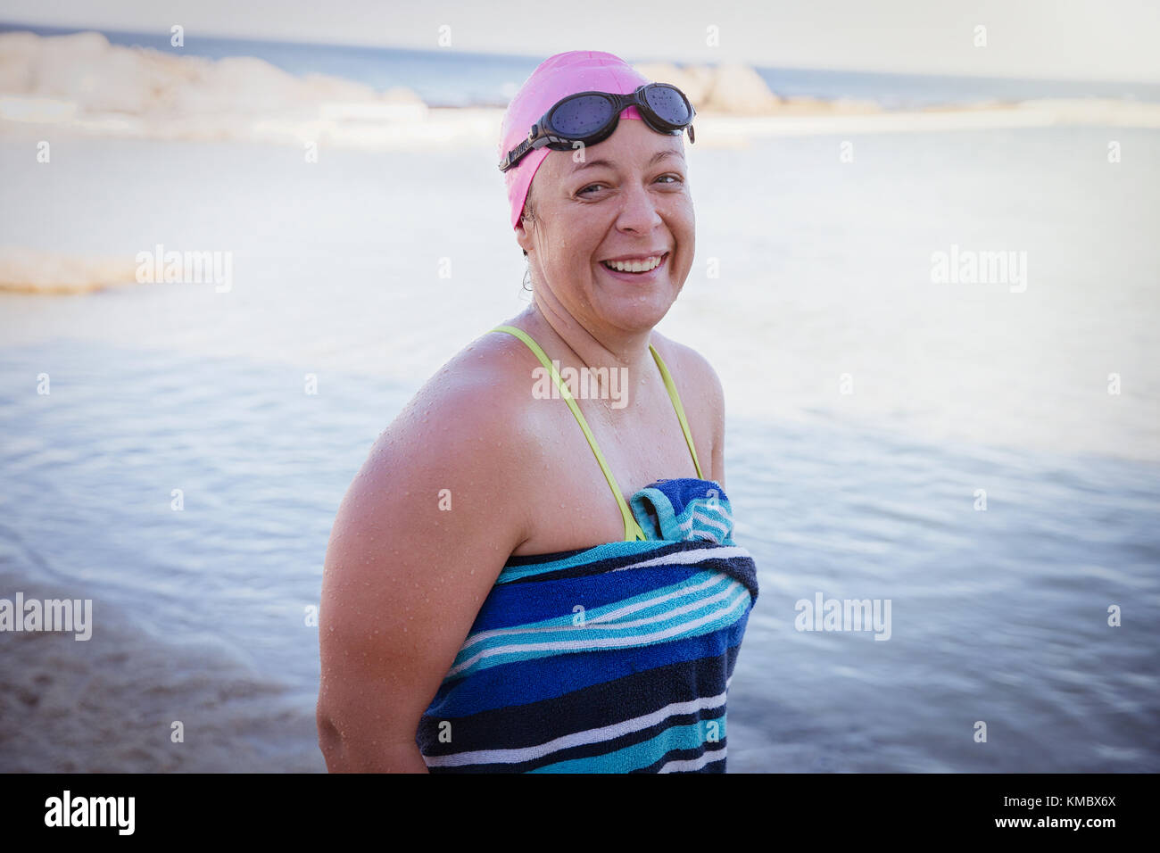 Ritratto sorridente nuotatore in acqua aperta avvolto in asciugamano sull'oceano spiaggia Foto Stock