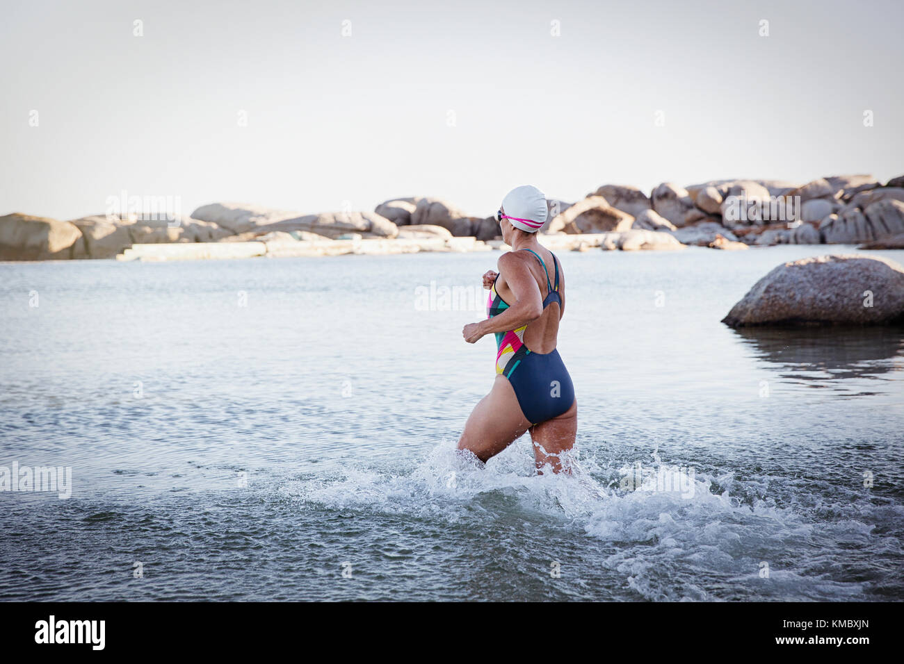 Nuotatore femminile in acqua aperta che corre e spruzzi nel surf oceanico Foto Stock