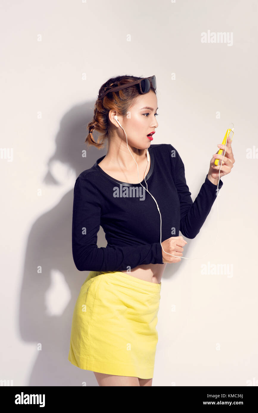 Giovane ragazza asiatica facendo emozione. vestito con una camicia nera ed il mantello giallo. colore caldo. sfondo bianco, non isolata Foto Stock