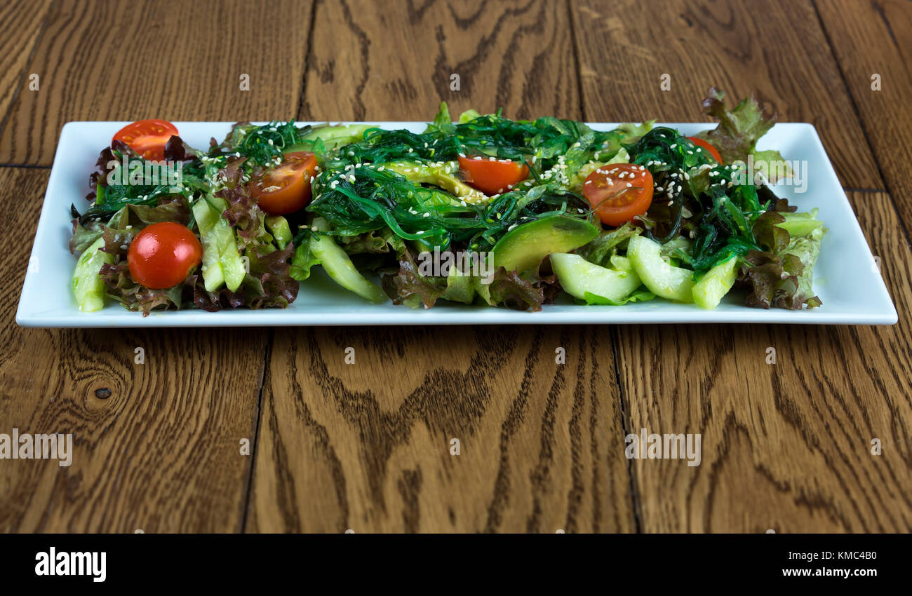 Fresco e salutare insalata di verdure con pomodori ciliegia, avocado, cetriolo, foglie verde su bianco piastra orizzontale, vista dall'alto, close-up su una superficie di legno Foto Stock