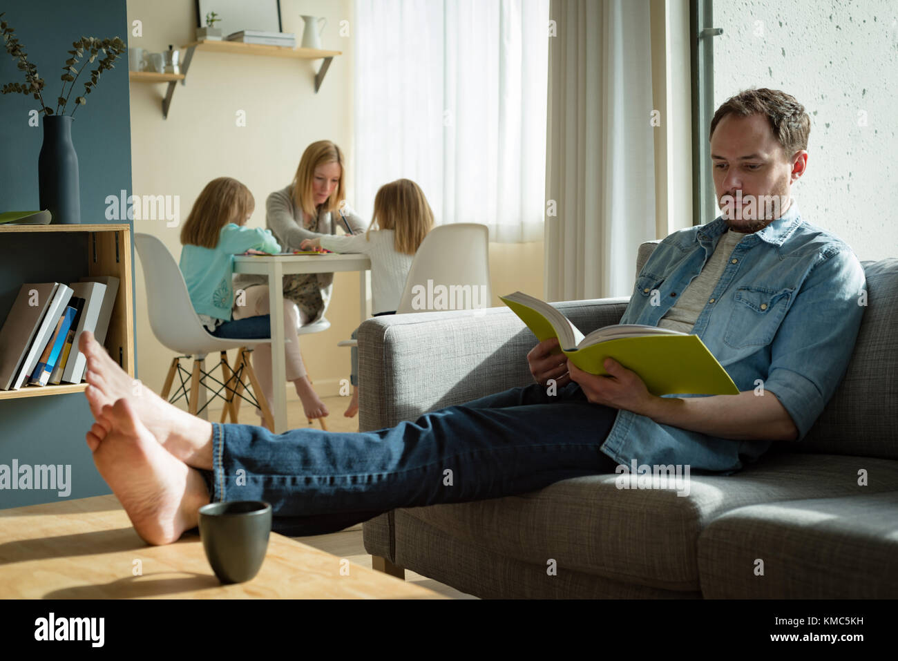 Padre che legge un libro mentre la madre che aiuta i suoi figli negli studi Foto Stock