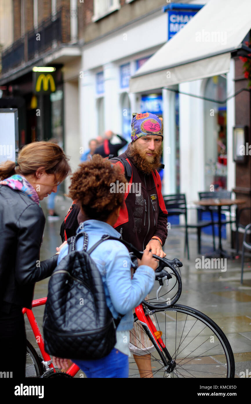 Barbuto ciclista indossando bandana spingendo la sua bicicletta sul marciapiede in London, England, Regno Unito Foto Stock