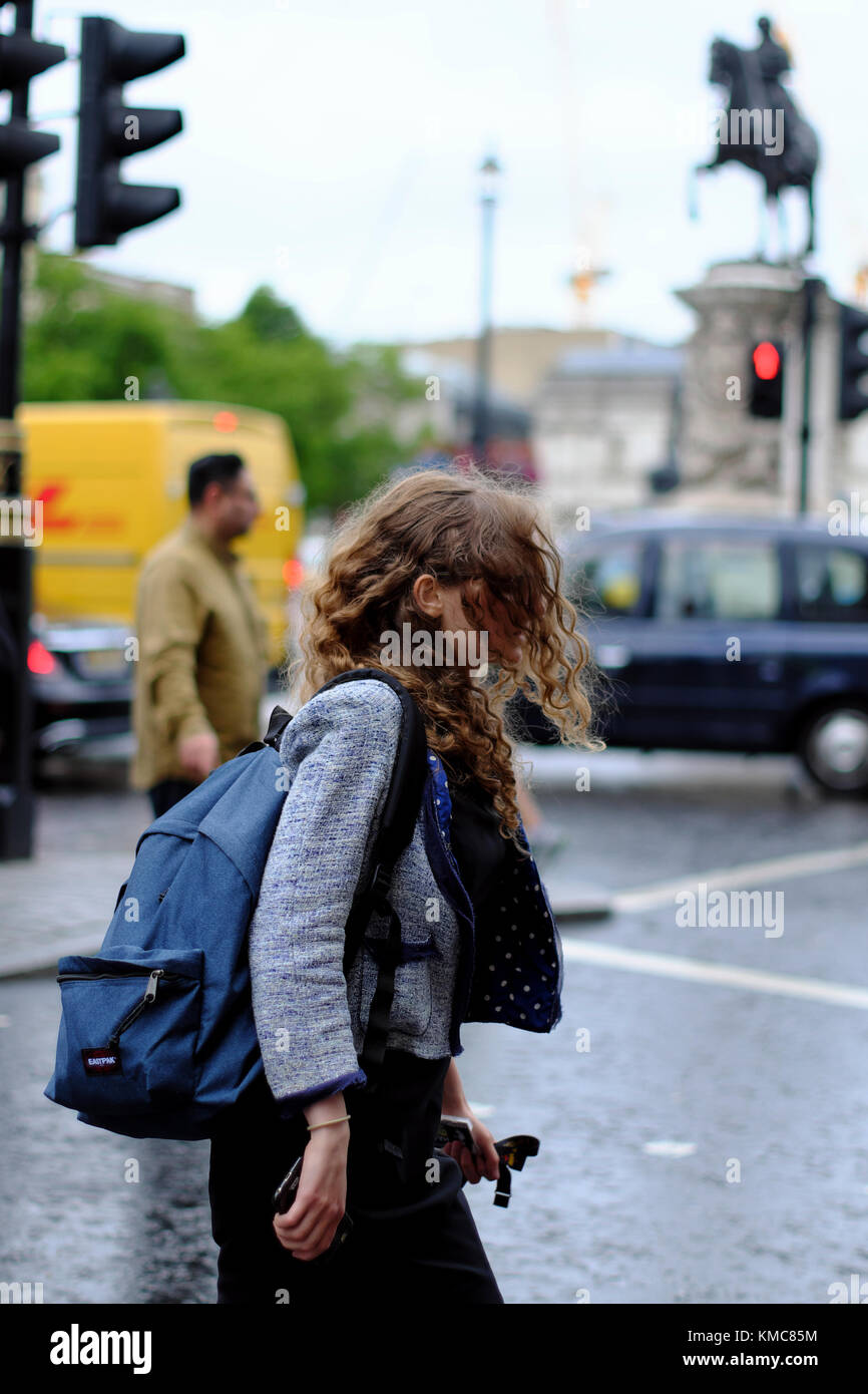 Bruna giovane donna con capelli spazzate dal vento su strada di attraversamento a Trafalgar Square a Londra, Inghilterra, Regno Unito Foto Stock