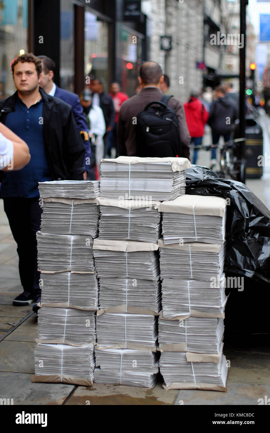 Quotidiani alta impilati sul pavimento con le persone camminare davanti a Londra, Inghilterra, Regno Unito Foto Stock
