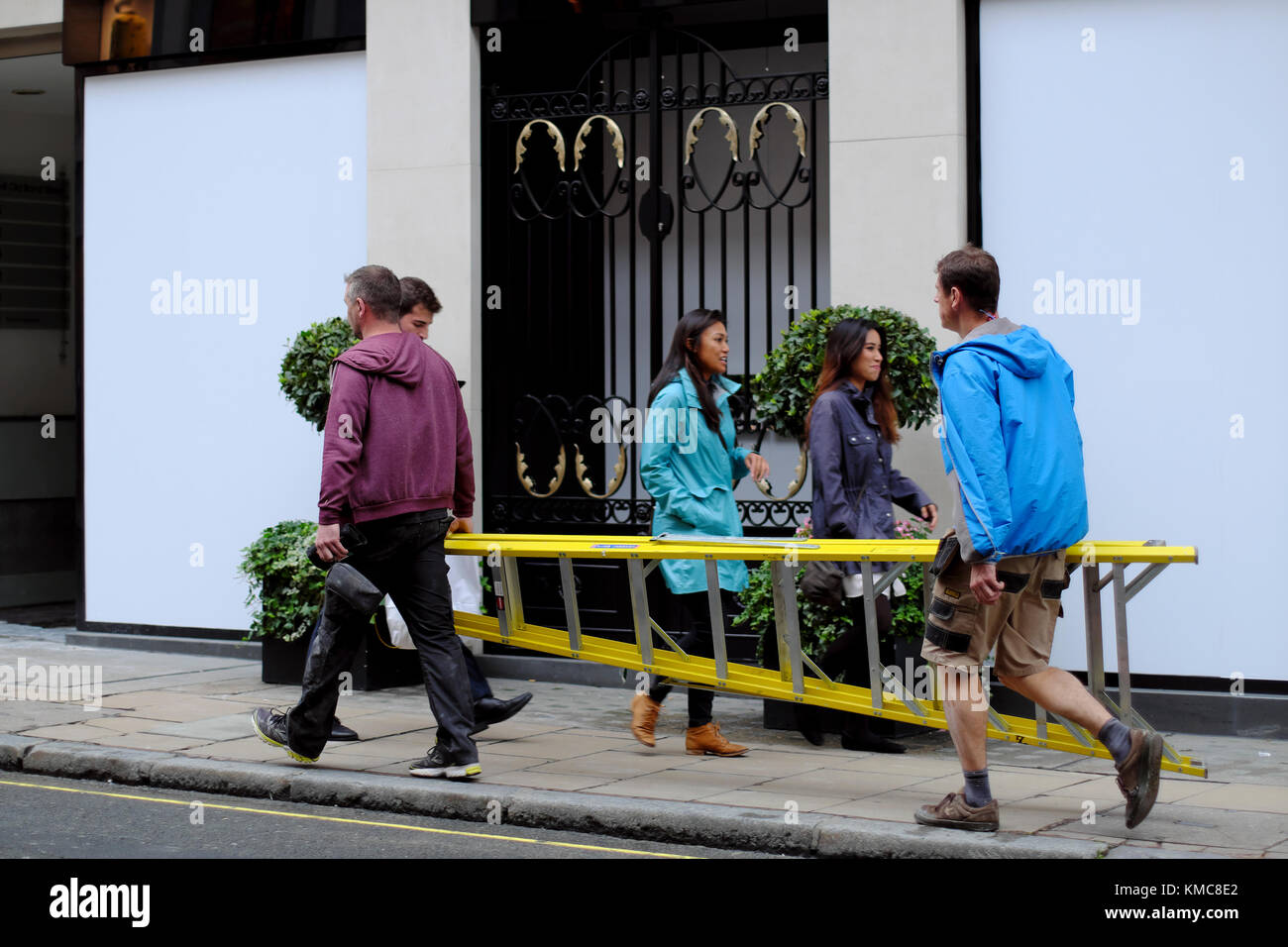 Operai che trasportano un alto scaletta passato gli acquirenti su Old Bond Street, Londra, Inghilterra, Regno Unito Foto Stock