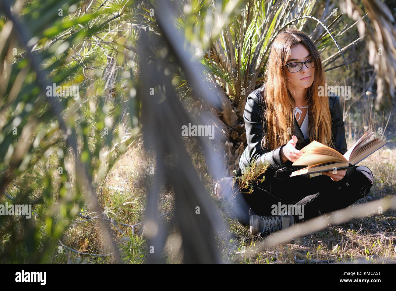 Giovani brunette leggendo un libro all'aperto Foto Stock