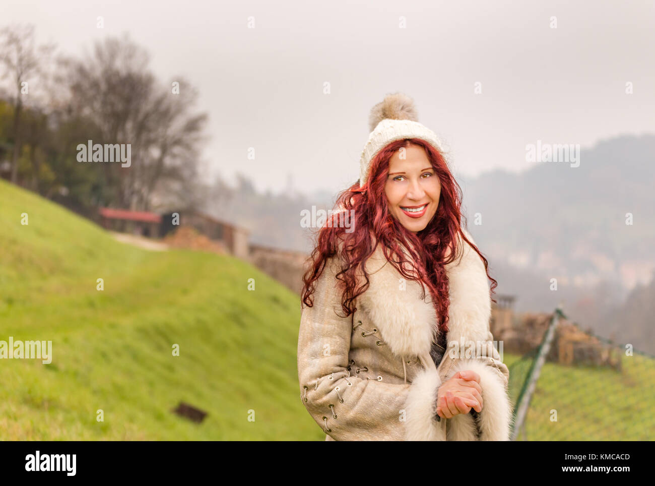 Donna matura con red cherry capelli indossare caldo pelliccia e sorridente nel paesaggio invernale pieno di gioia di vivere il cambiamento di vita della menopausa Foto Stock