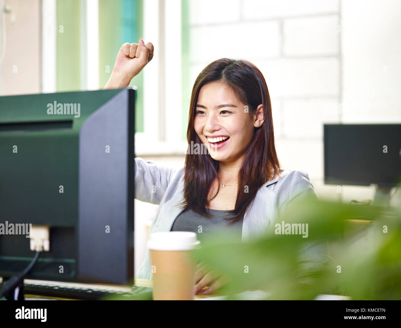 Giovani asian business donna che lavorano in ufficio utilizzando il computer desktop, felice ed entusiasta di buone notizie. Foto Stock