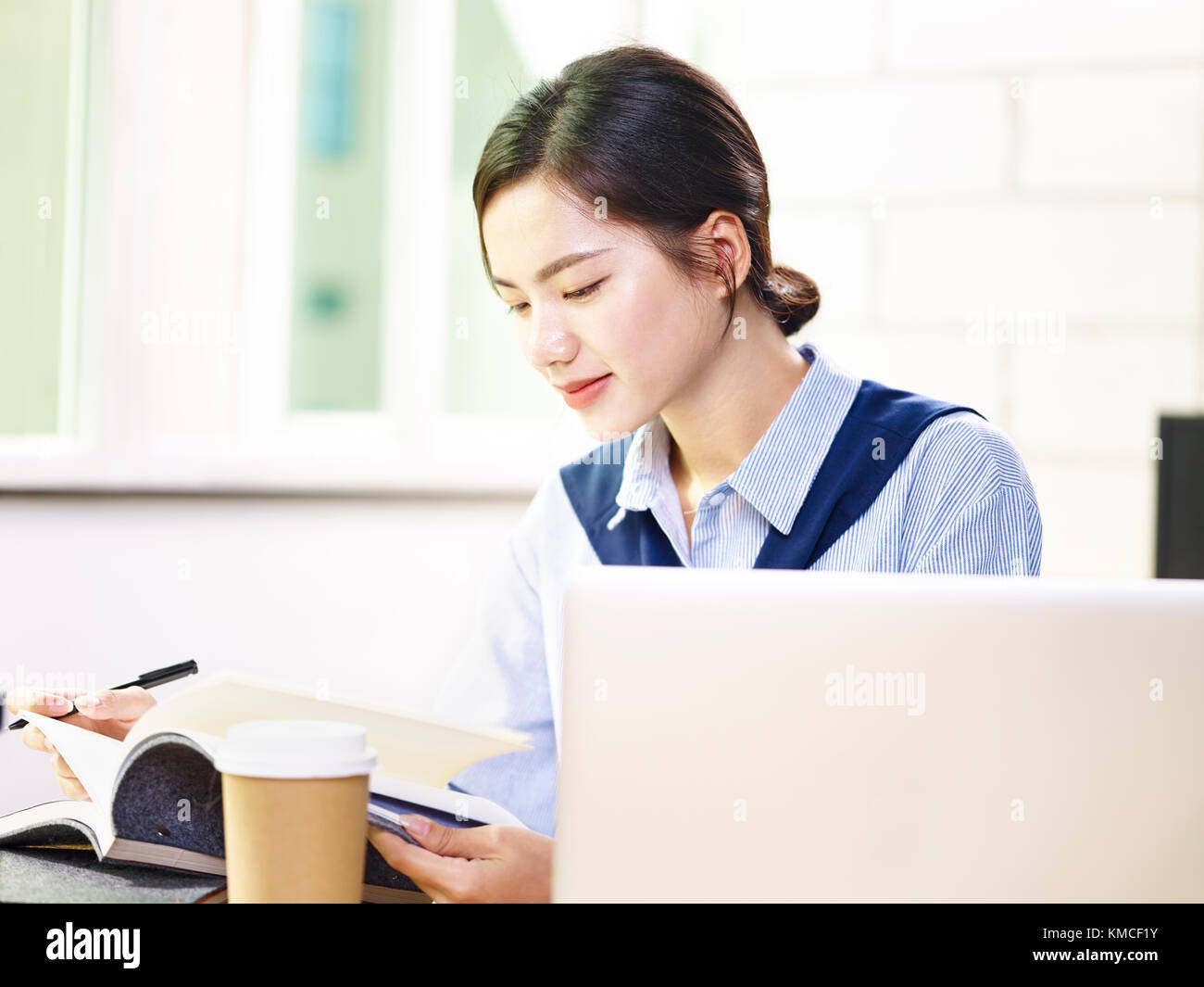 Giovani asian business donna note di controllo mentre si lavora in ufficio utilizzando il computer portatile. Foto Stock