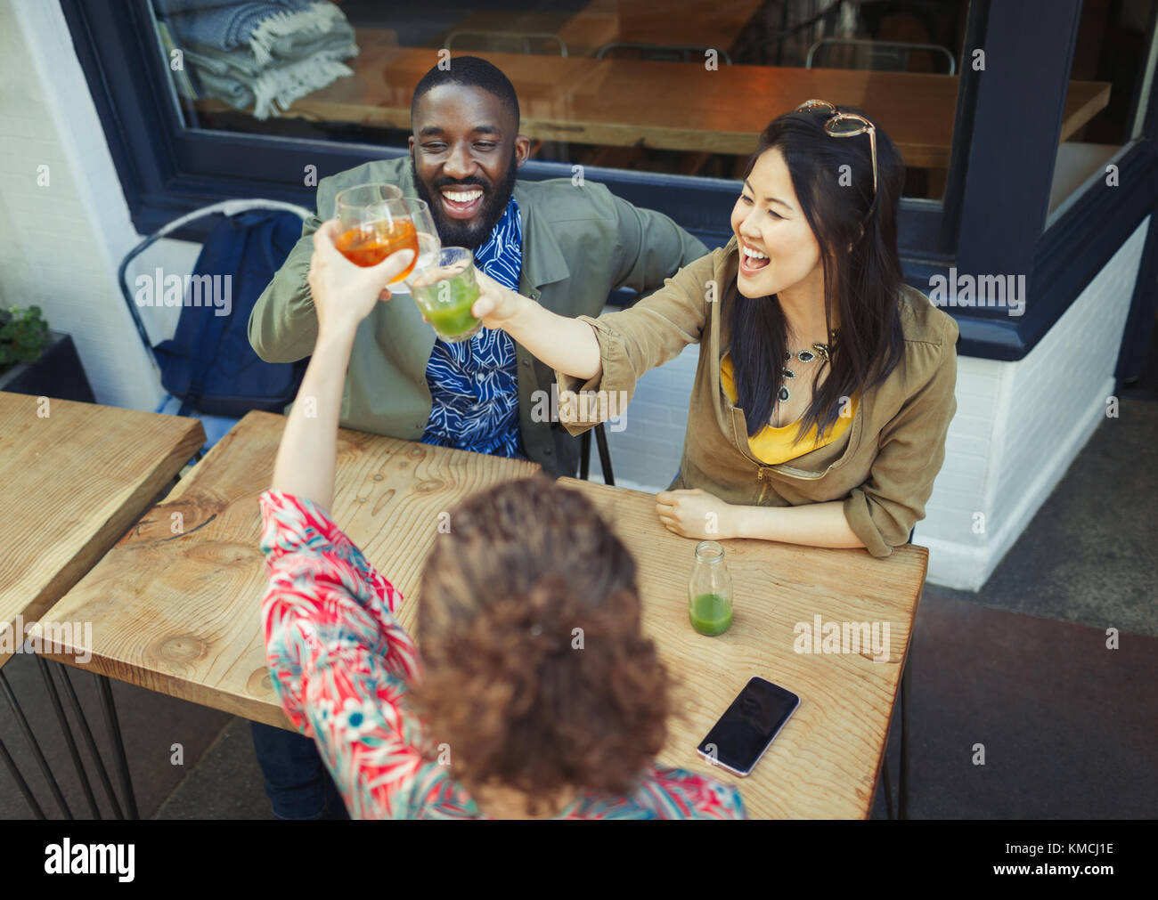 Amici entusiasti che tostano bicchieri di succo fresco al bar Sidewalk Foto Stock