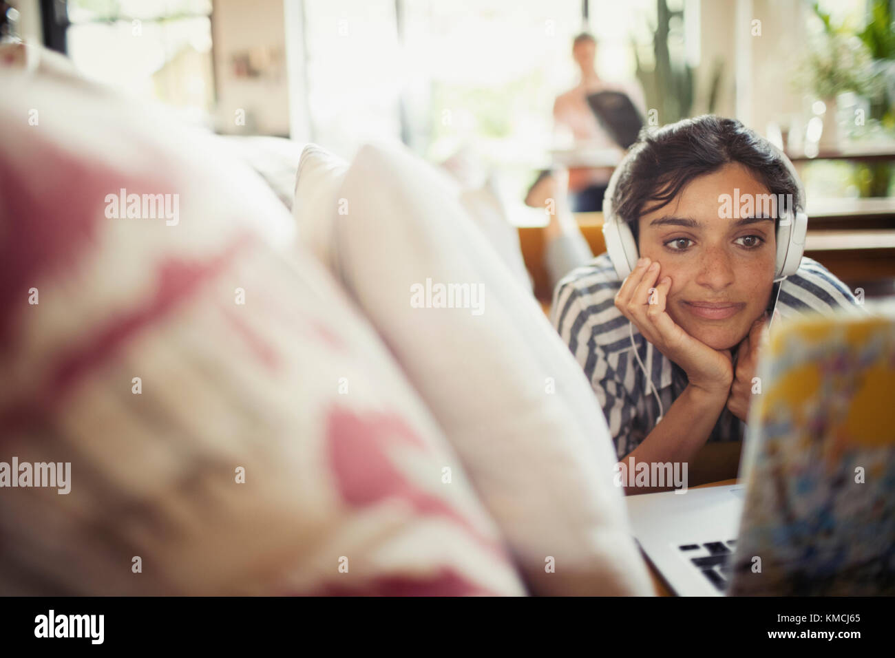 Giovane donna con cuffie che usano il computer portatile sul divano del soggiorno Foto Stock