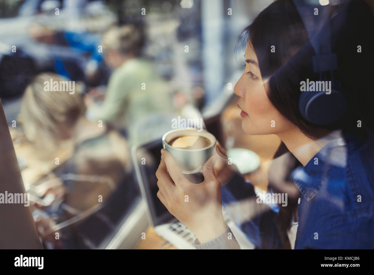 Giovane donna che ascolta la musica con le cuffie e beve caffè alla caffetteria Foto Stock