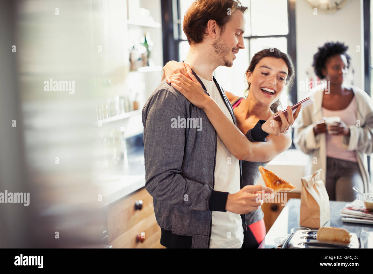 Affettuosa giovane costeggiata, sms con smart phone in cucina Foto Stock