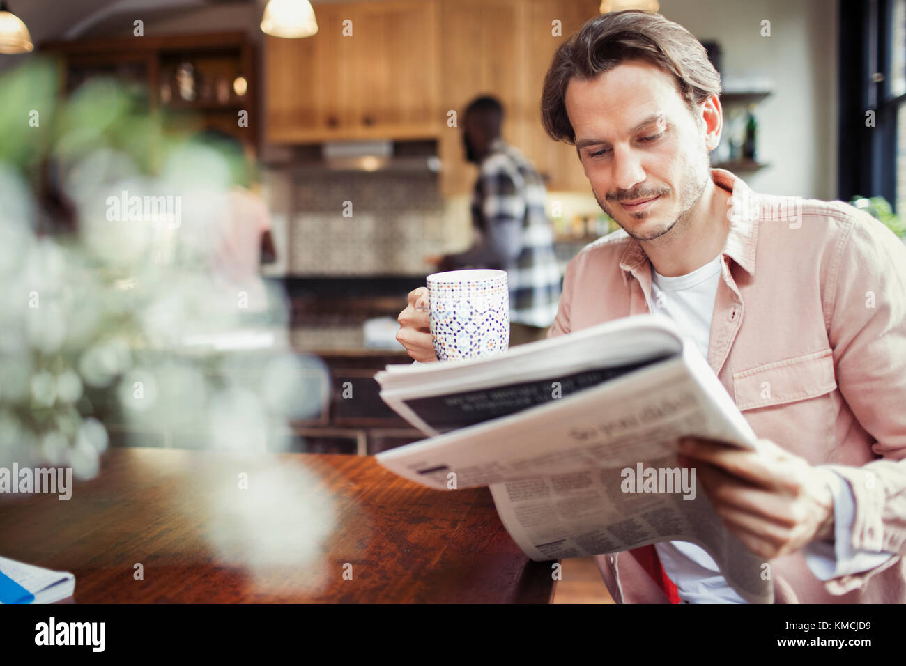 Uomo che beve caffè e lettura giornale in cucina Foto Stock