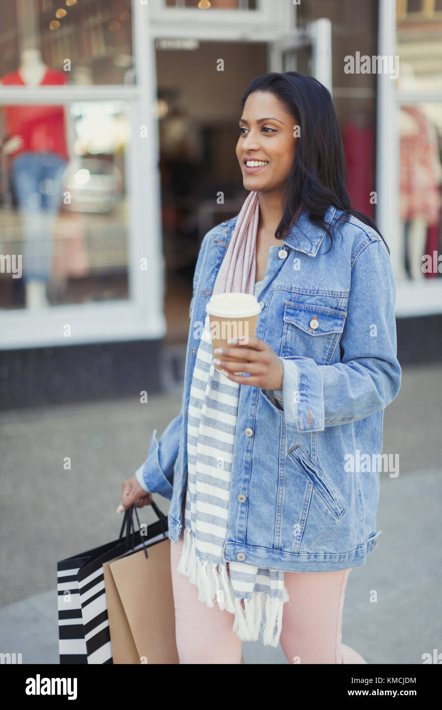 Donna sorridente che cammina lungo il negozio con caffè e borse per lo shopping Foto Stock