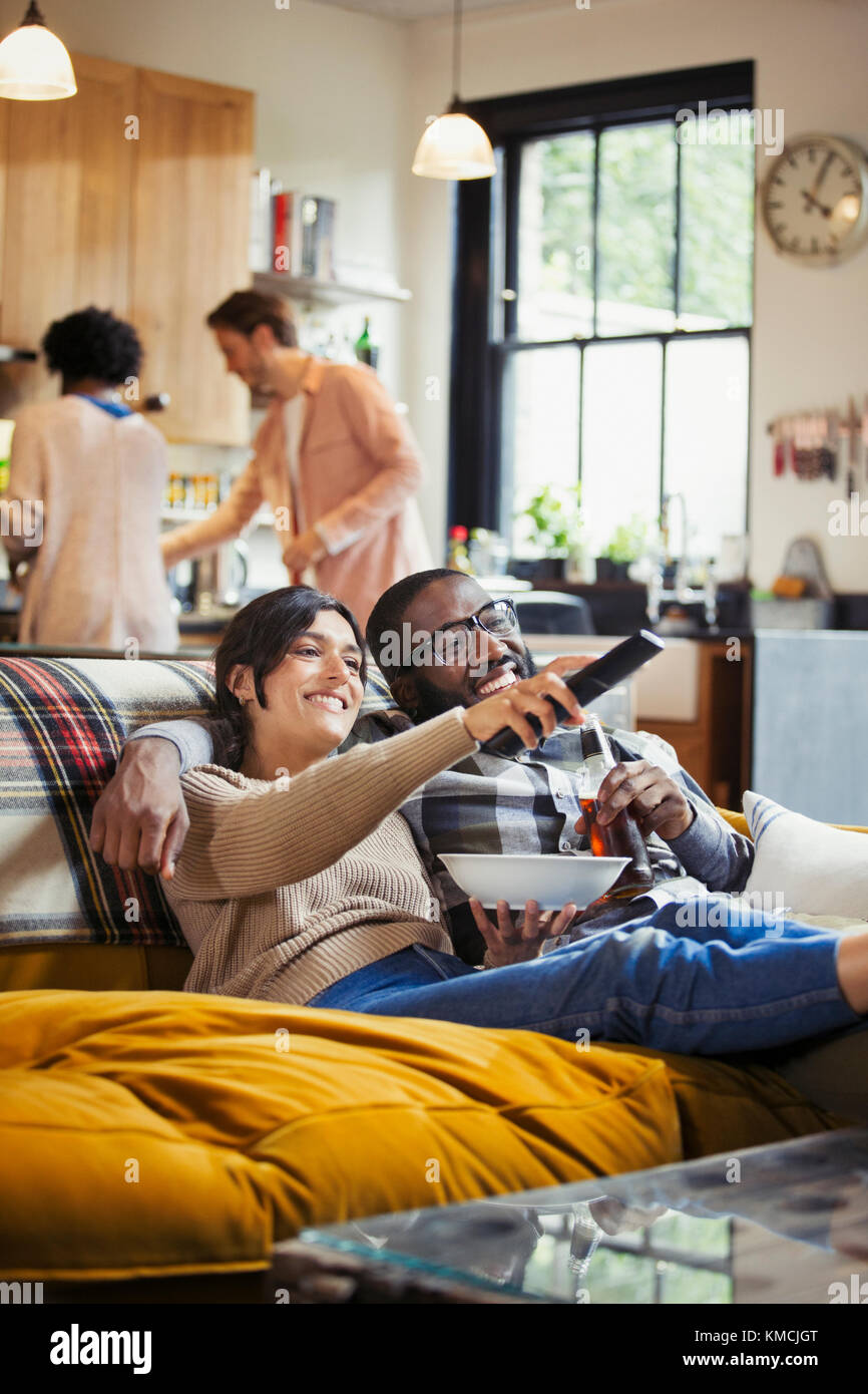 Coppia sorridente e affettuosa che guarda la TV e che mangia popcorn sul divano del soggiorno Foto Stock