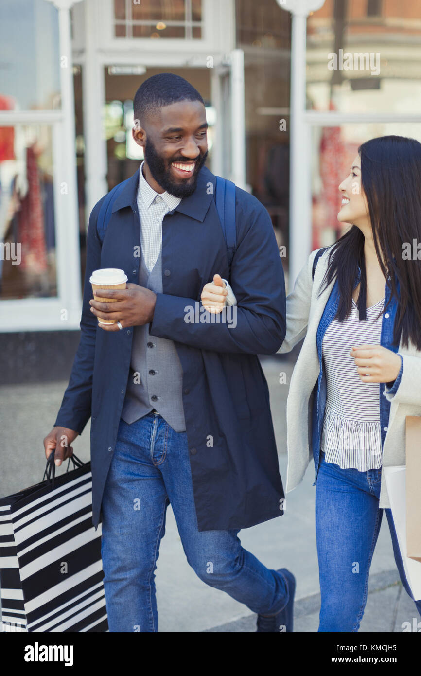 Giovane coppia sorridente che cammina lungo il negozio con caffè e shopping borse Foto Stock