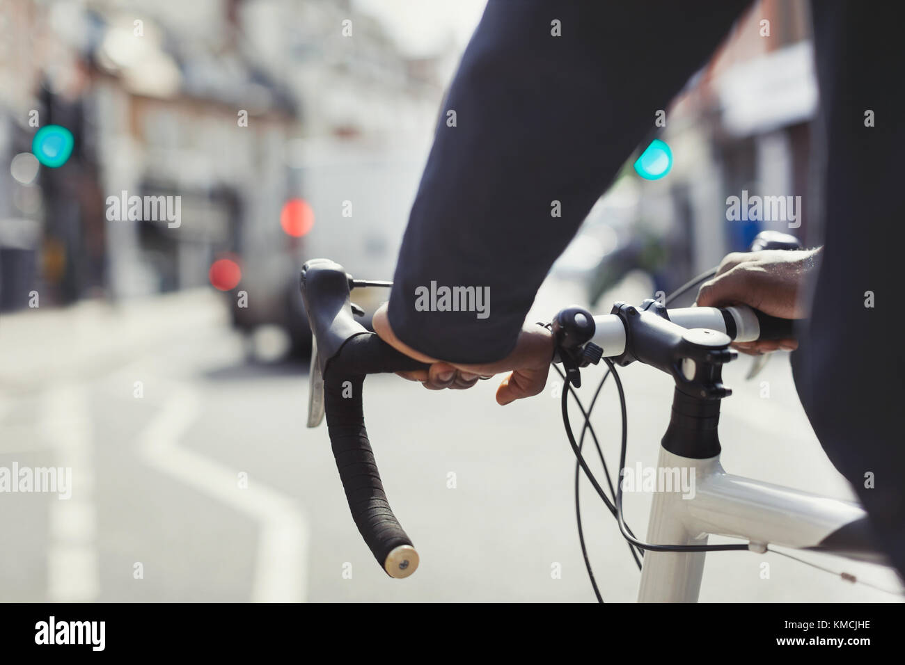 Mani sull'uomo sul manubrio della bicicletta, che si trova in una strada urbana soleggiata Foto Stock