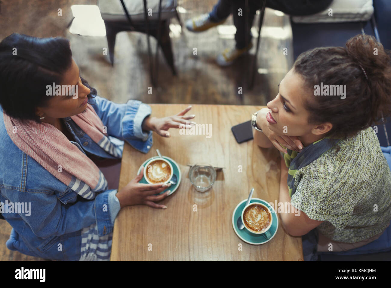Giovani donne amici che parlano e bevono cappuccini al tavolo del caffè Foto Stock