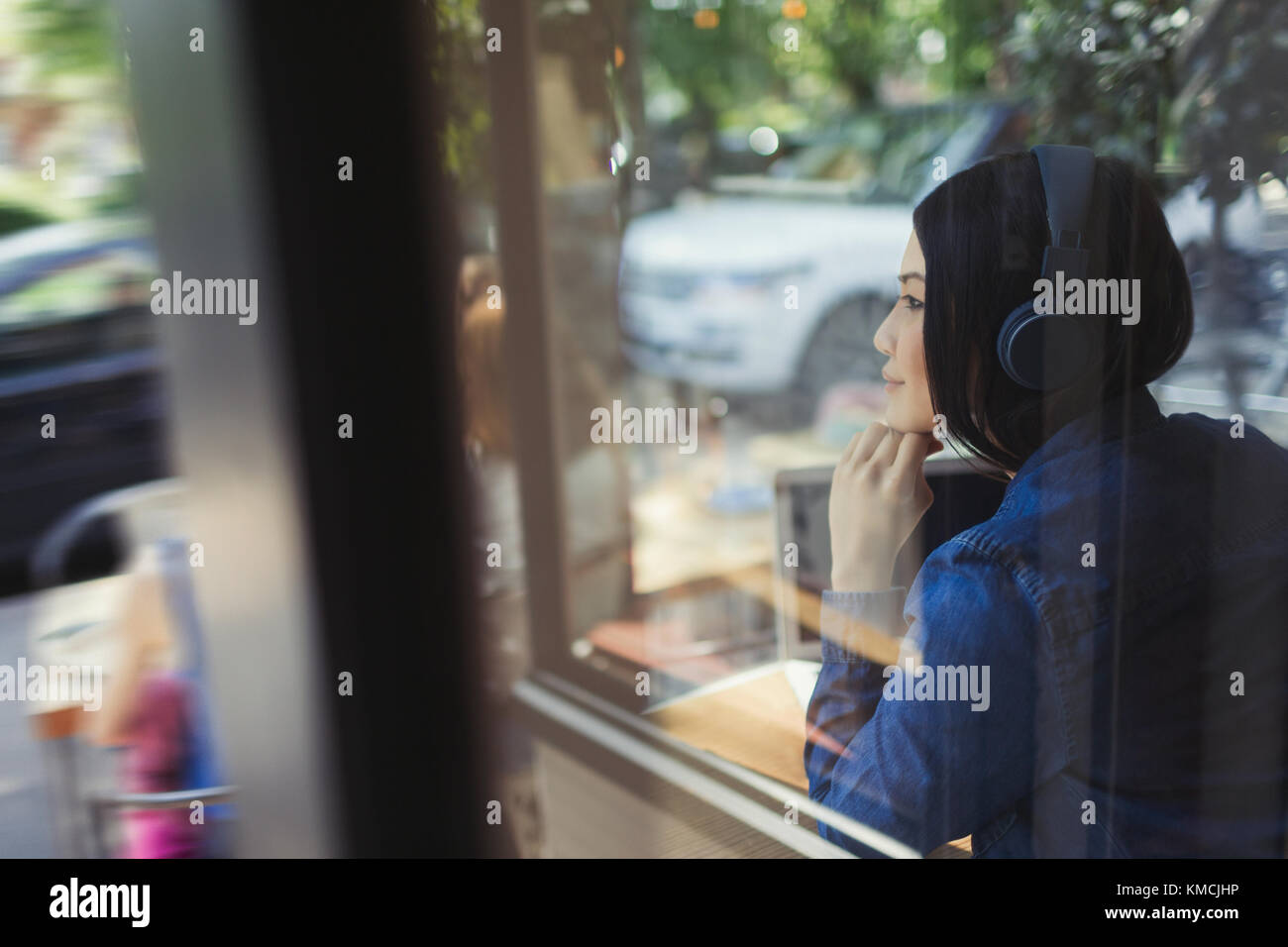 Giovane donna che ascolta la musica con le cuffie che guardano lontano alla finestra del caffè Foto Stock