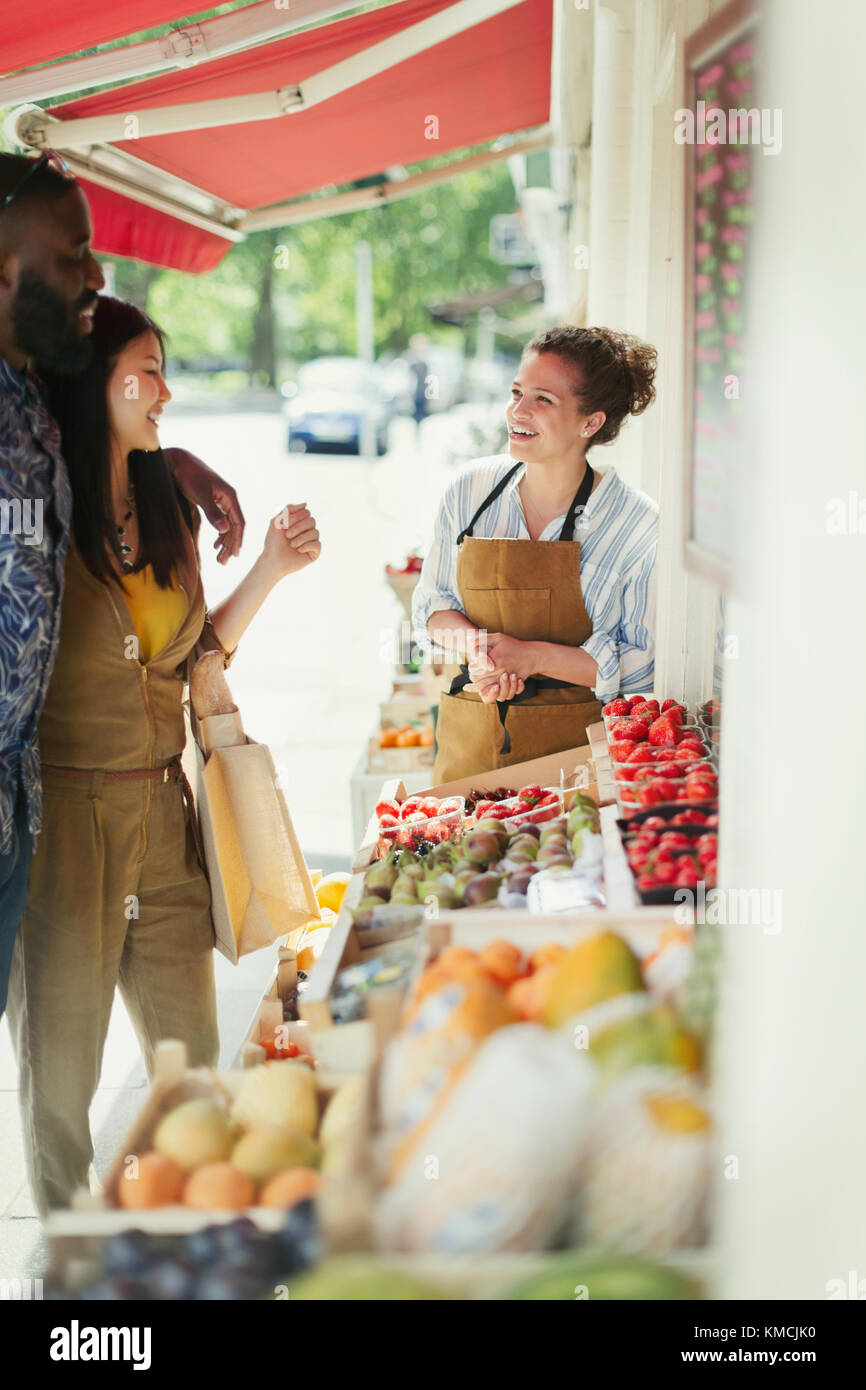 Lavoratrice femminile che aiuta la giovane coppia a fare acquisti di frutta sul mercato storefront Foto Stock