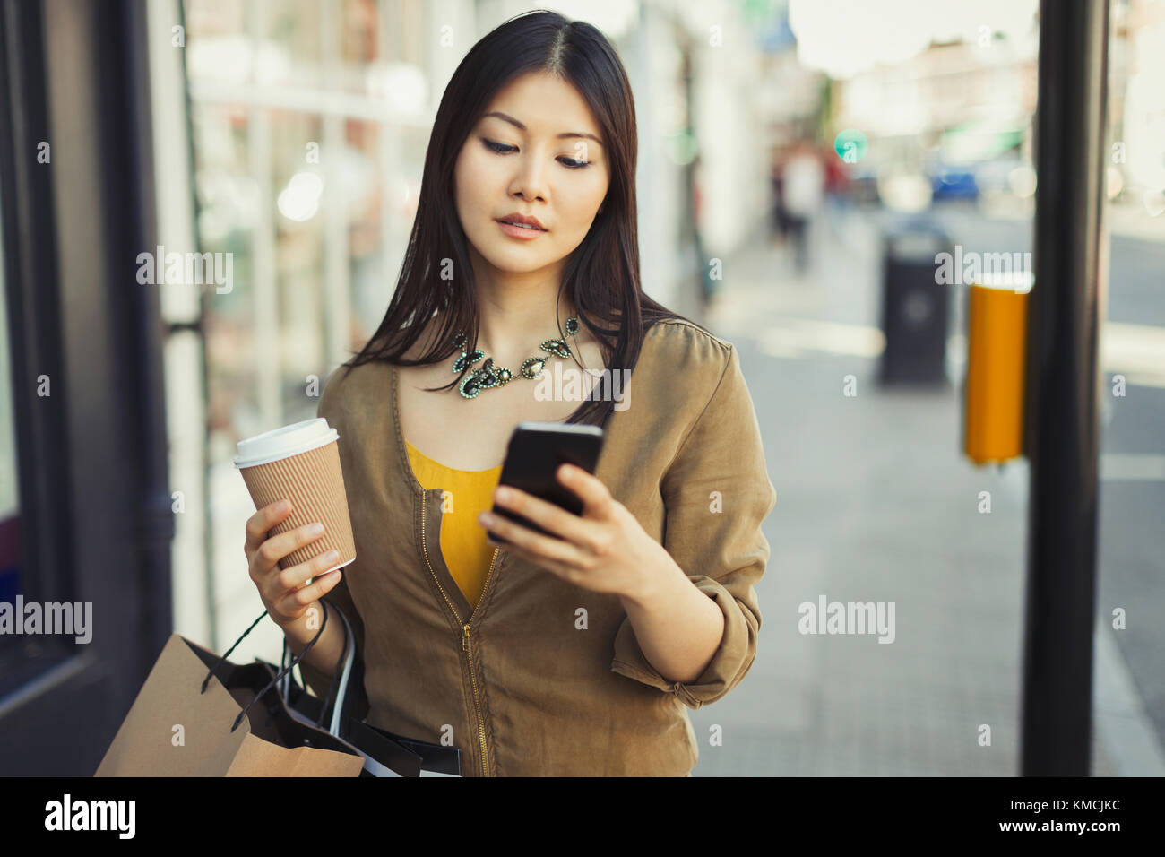 Giovane donna con caffè testing con cellulare su urbano marciapiede Foto Stock