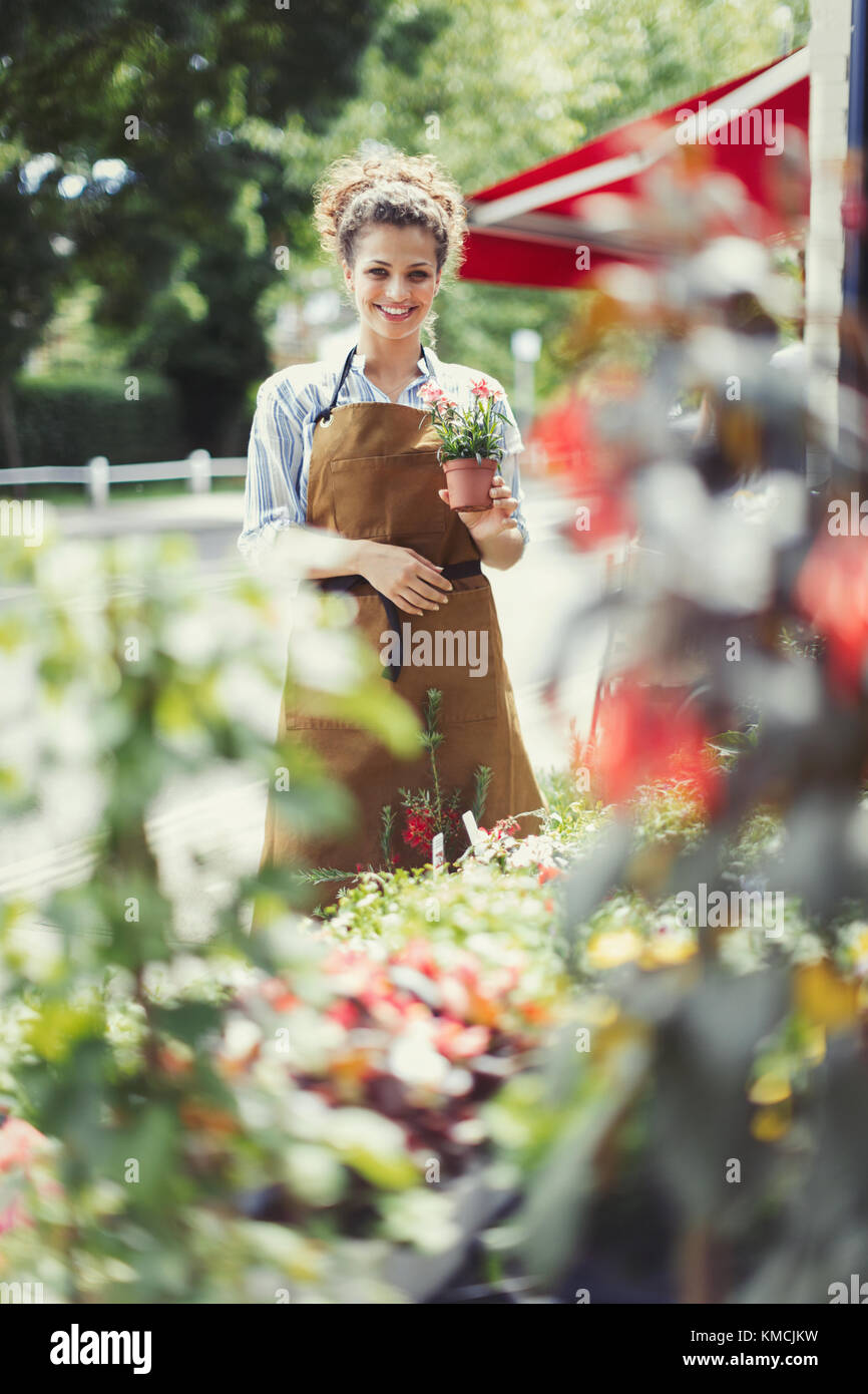 Ritratto sorridente fiorista femminile che tiene in vaso la pianta al negozio di fiori storefront Foto Stock
