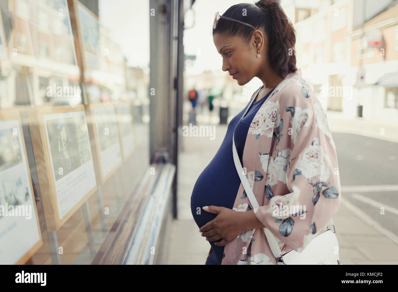 Donna incinta che sta navigando gli elenchi immobiliari a Urban storefront Foto Stock