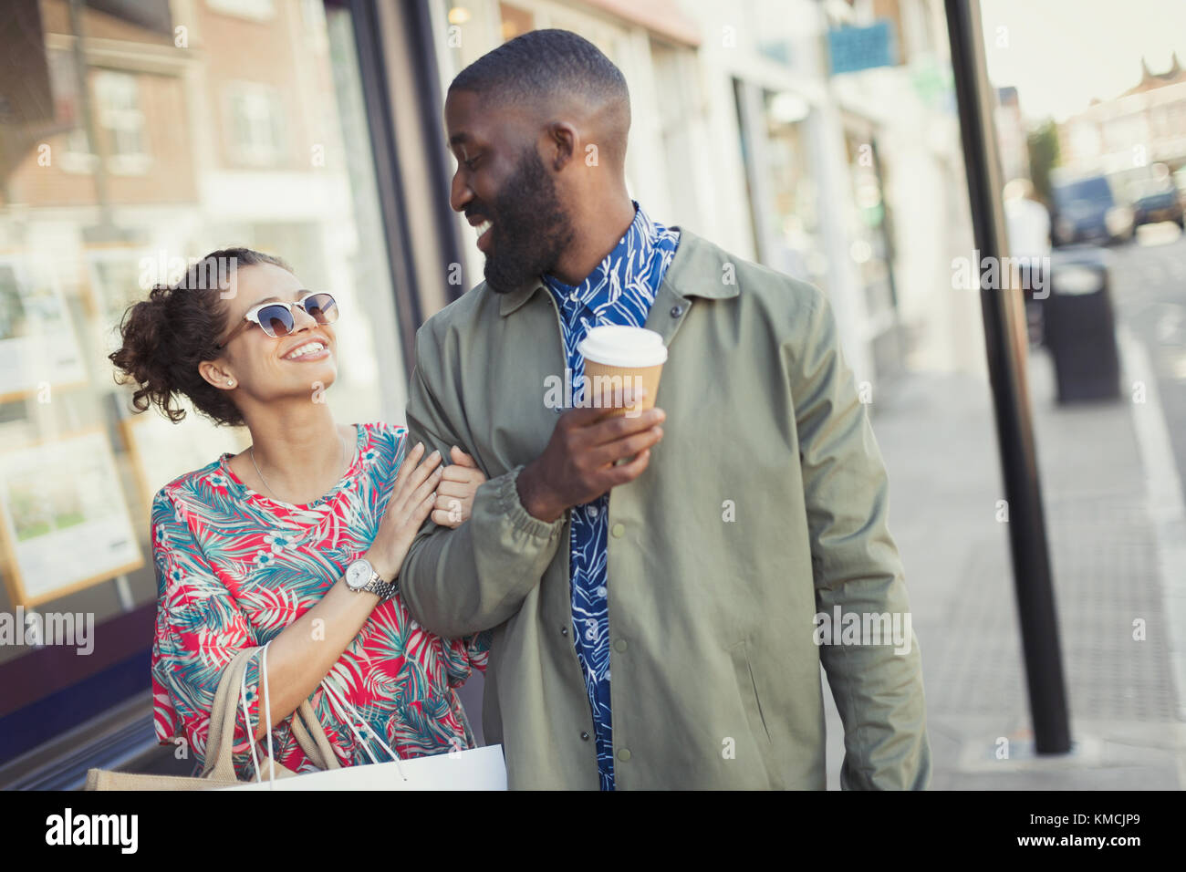 Giovane coppia sorridente con il braccio per camminare con il caffè nel braccio lungo storefronts Foto Stock
