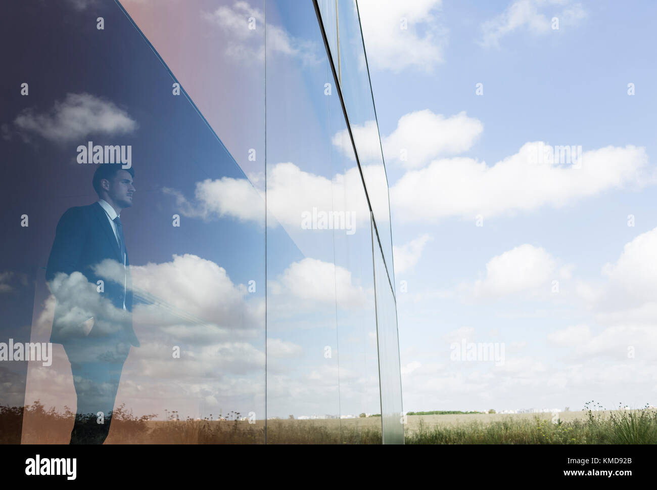 Uomo d'affari pensivo che guarda verso l'esterno la moderna finestra dell'ufficio al cielo blu e nuvole Foto Stock