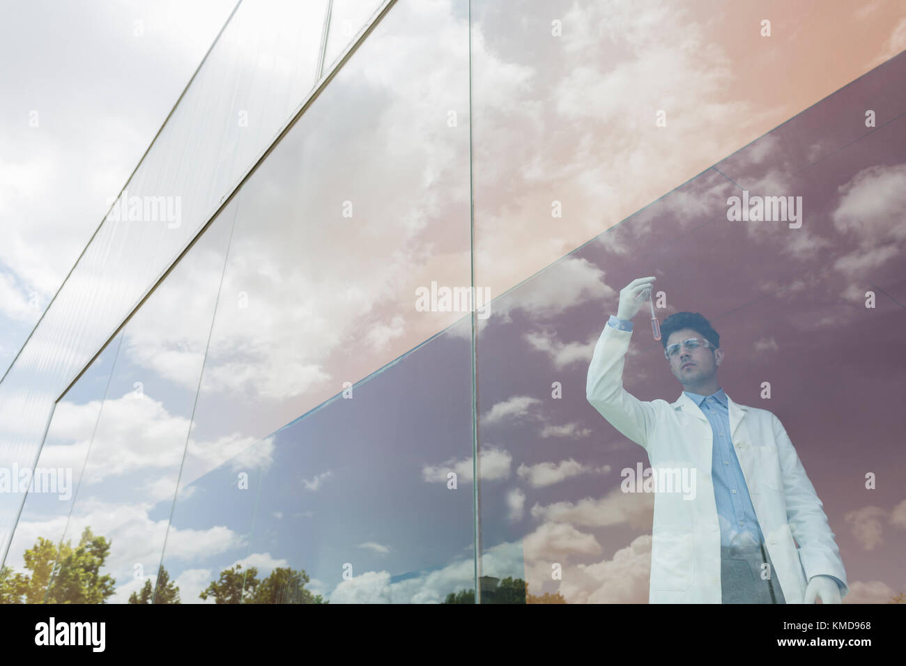 Scienziato che esamina il liquido in becher alla finestra moderna con la nuvola riflessioni Foto Stock