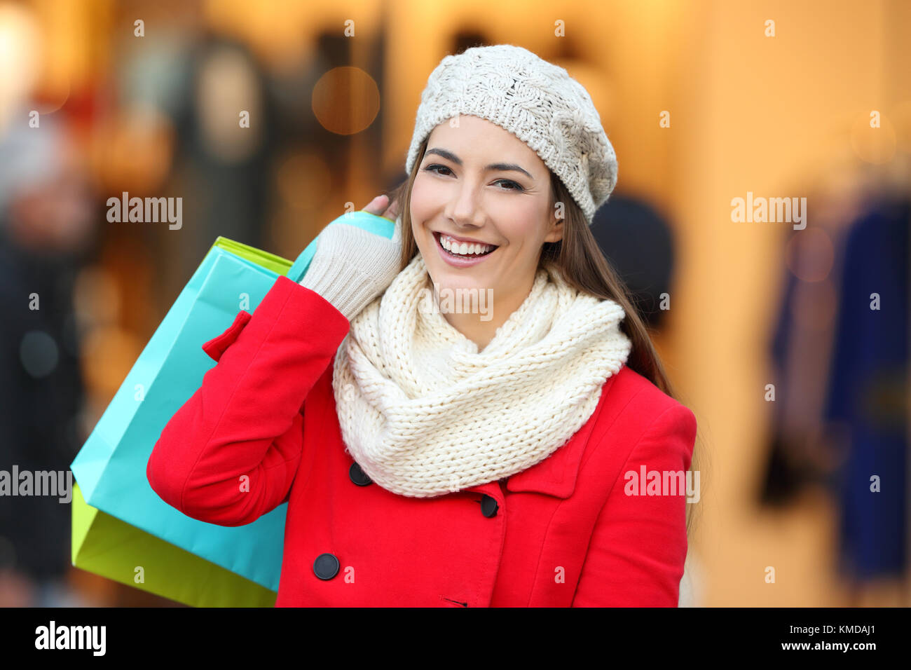 Vista anteriore verticale di un felice shopper indossando cappotto rosso azienda shopping bags guardando a voi in un centro commerciale di inverno Foto Stock